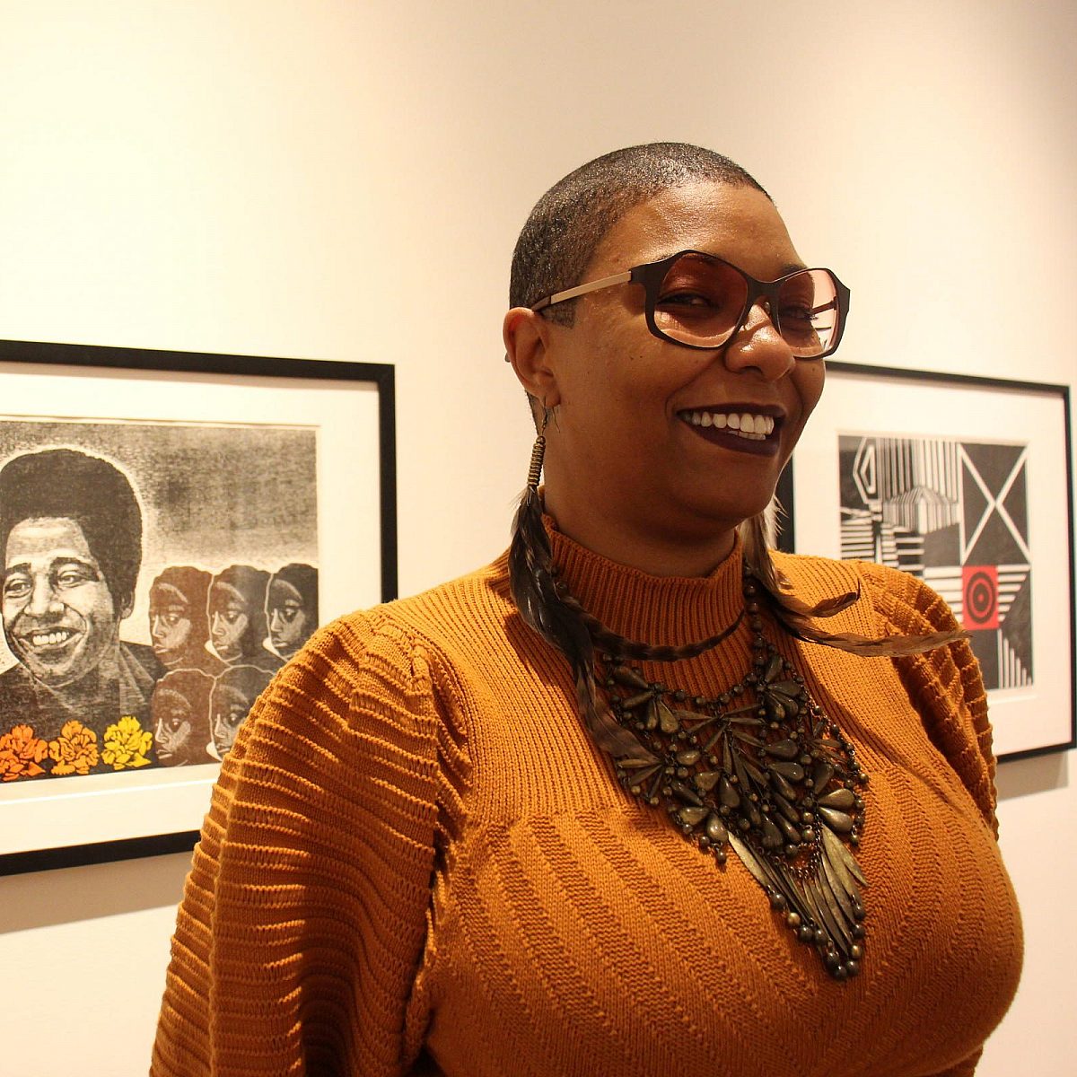 Black woman standing in front of print work in gallery, looking off camera